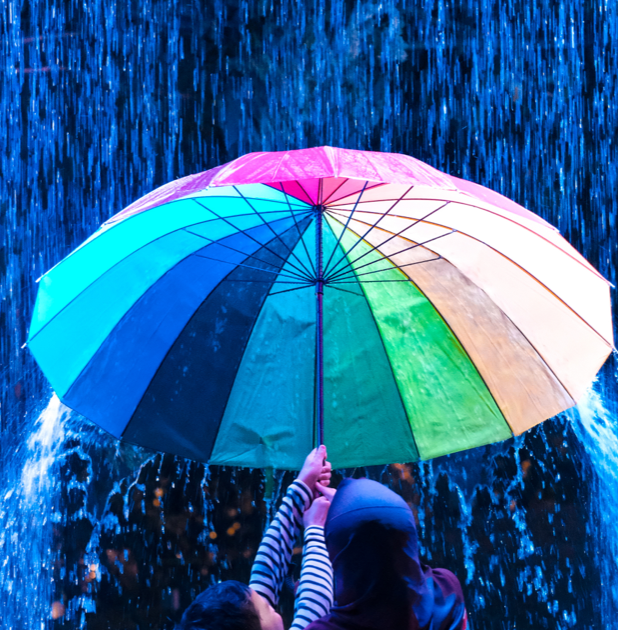 Two people holding a multicolored umbrella under falling water