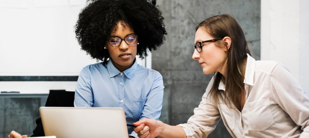 Two female employees looking at laptop while solving a business challenge